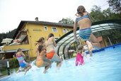 Einige Kinder springen in den Outdoor-Pool im Kinderhotel Bruckwirt in Oberösterreich