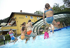 Einige Kinder springen in den Outdoor-Pool im Kinderhotel Bruckwirt in Oberösterreich