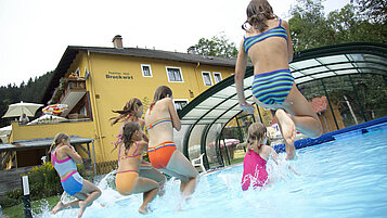 Einige Kinder springen in den Outdoor-Pool im Kinderhotel Bruckwirt in Oberösterreich