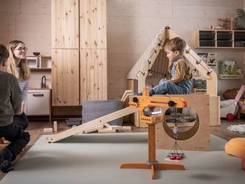Kinder spielen im gemütlichen Indoor-Spielzimmer mit Holzhaus und Baukran im Familienhotel Elldus im Erzgebirge.
