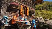 Familie beim Brotzeit machen auf einer Kärntner Berghütte.