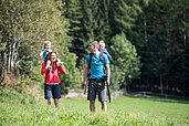 Familie mit zwei Kleinkindern beim Wandern durch die sommerliche Natur in Südtirol.