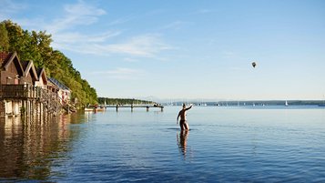 Frau geht ins Wasser mit Hütten am Ufer.
