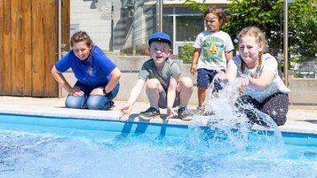 Kinder planschen gemeinsam mit einer Kundenbetreuerin im Wasser des Outdoor Pools im Family Club Harz 