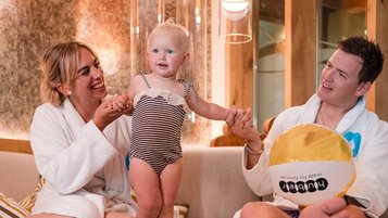 Eltern entspannen mit ihrem Kleinkind in Bademänteln im Wellnessbereich des Familienhotels Huber in Südtirol und genießen gemeinsame Wohlfühlzeit.