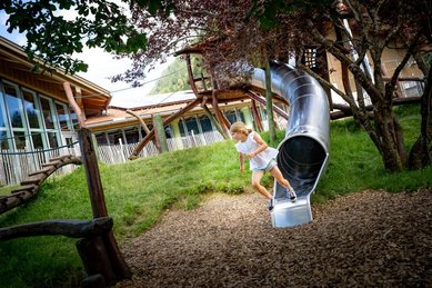Mädchen rutscht lachend aus einer Edelstahlrutsche beim großen Kletterturm im Familienhotel Krone im Allgäu.