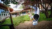 Mädchen rutscht lachend aus einer Edelstahlrutsche beim großen Kletterturm im Familienhotel Krone im Allgäu.