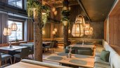 Gemütlicher Restaurantbereich im Zauchenseehof mit warmem Holzdesign, Baumstamm-Elementen, hängenden Korbleuchten und einladenden Sitznischen.