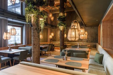 Gemütlicher Restaurantbereich im Zauchenseehof mit warmem Holzdesign, Baumstamm-Elementen, hängenden Korbleuchten und einladenden Sitznischen.