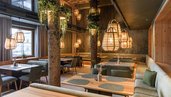 Gemütlicher Restaurantbereich im Zauchenseehof mit warmem Holzdesign, Baumstamm-Elementen, hängenden Korbleuchten und einladenden Sitznischen.