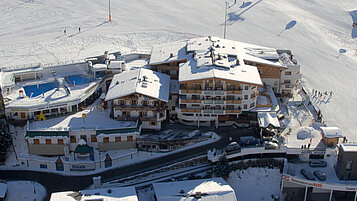 Winter-Luftaufnahme vom Wellness- & Familienhotel Egger in Saalbach Hinterglemm mit Skipiste.