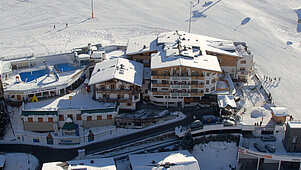 Winter-Luftaufnahme vom Wellness- & Familienhotel Egger in Saalbach Hinterglemm mit Skipiste.