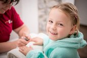 Glückliches Mädchen im flauschigen Bademantel genießt eine liebevolle Maniküre im Wellnessbereich des Landguts Furtherwirt
