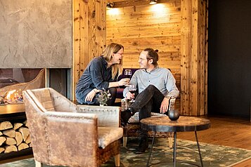 Eltern sitzen mit einem Glas Rotwein in der Hand in der gemütlichen Lounge des Familienhotels Sonnenpark.