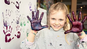 Ein fröhliches Mädchen im Familienhotel zeigt stolz ihre bunten Hände nach einer kreativen Malaktion