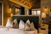 Gemütliches Schlafzimmer im Alpura Retreat mit Holzwänden, großen Fenstern, Hirschgeweih an der Wand und stilvoll dekoriertem Bett.