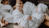 Eine Familie liegt in Bademänteln im Familienhotel Mia Alpina in Tirol gemeinsam auf einem Bett und kuschelt.