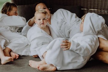 Eine Familie liegt in Bademänteln im Familienhotel Mia Alpina in Tirol gemeinsam auf einem Bett und kuschelt.