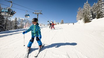Ein Kind fährt im Winterurlaub eine Skipiste hinunter