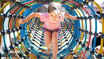 Mädchen spielt in einem Kletternetz auf dem Outdoor-Spielplatz des Familienhotels Adler in Tirol.