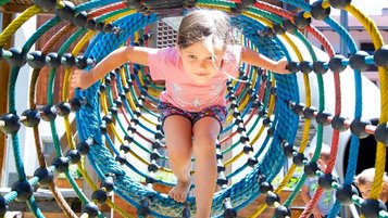Mädchen spielt in einem Kletternetz auf dem Outdoor-Spielplatz des Familienhotels Adler in Tirol.