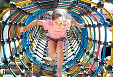 Mädchen spielt in einem Kletternetz auf dem Outdoor-Spielplatz des Familienhotels Adler in Tirol.