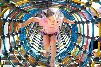 Mädchen spielt in einem Kletternetz auf dem Outdoor-Spielplatz des Familienhotels Adler in Tirol.