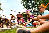 Kinder sitzen um ein Lagerfeuer mit Stockbrot im Familienhotel Amiamo im Salzburger Land