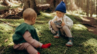 Zwei Kleinkinder sitzen im Wald auf Moos.
