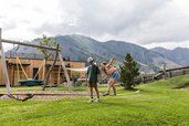 Kinder spielen auf dem Spielplatz mit Schaukel und Slackline im Familienhotel Almfamilyhotel Scherer inmitten der Osttiroler Berge.