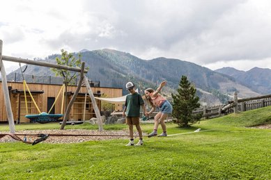 Kinder spielen auf dem Spielplatz mit Schaukel und Slackline im Familienhotel Almfamilyhotel Scherer inmitten der Osttiroler Berge.