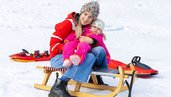 Mutter fährt mit ihrem Kind schlitten im Winter.