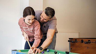 Vater spielt mit seiner Tochter Billard im Familienhotel Alpenhotel Kindl in Tirol.