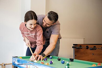 Vater spielt mit seiner Tochter Billard im Familienhotel Alpenhotel Kindl in Tirol.