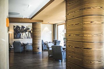 Moderne Hotelbar im Familienhotel Alpenhof im Allgäu, gekennzeichnet durch stilvolle Sitzmöbel, elegante Holzsäulen und warme Beleuchtung, die eine gemütliche Atmosphäre für Gäste schafft.