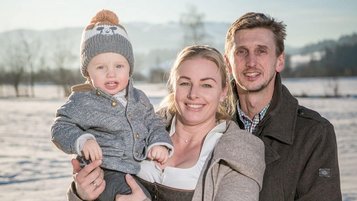 Gastgeberfamilie des Familienhotel Furtherwirt steht im verschneiten Winterpanorama und lächelt in die Kamera.