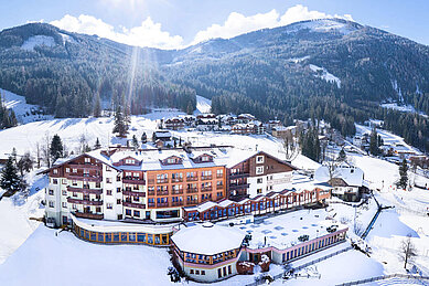 Das Familienhotel Kirchheimerhof in Kärnten, umgeben von einer großen Hotel-Außenanlage und winterlichen Berglandschaft.