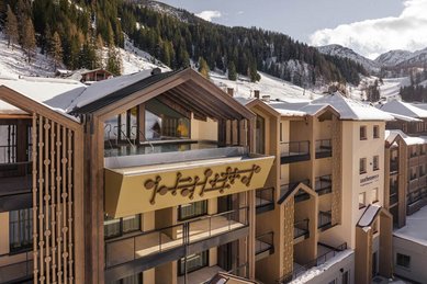 Außenansicht des Zauchenseehof: Das Hotel liegt eingebettet in eine verschneite Berglandschaft, mit einem modernen Gebäudeteil und einem spektakulär auskragenden Rooftop-Pool unter einem offenen Satteldach, der freien Blick auf die Skipisten bietet.
