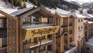 Außenansicht des Zauchenseehof: Das Hotel liegt eingebettet in eine verschneite Berglandschaft, mit einem modernen Gebäudeteil und einem spektakulär auskragenden Rooftop-Pool unter einem offenen Satteldach, der freien Blick auf die Skipisten bietet.