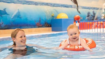 Mutter planscht mit ihrem Baby, das in einem Babyschwimmreifen sitzt, im Kinderpool des Familienhotels Kaiserhof in Tirol.