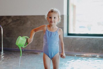Ein Kleinkind steht mit einer Gießkanne im Babybecken des Familienhotels Oberkarteis im Salzburger Land.