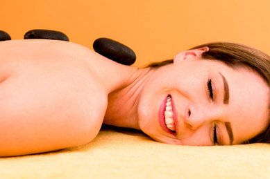 Eine Frau genießt eine entspannende Hot-Stone-Massage im Familienhotel Ramsi und lächelt mit geschlossenen Augen