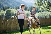 Ein kleienr Junge sitzt auf dem Pony und wird von einer Betreuerin geführt im Familienhotel Alphotel Tyrol Wellness & Family Resort in Südtirol.