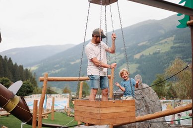 Vater und Sohn spielen auf dem Außenspielplatz vom Familotel Habachklause mit dem Seilzug