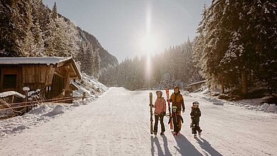 Eine Familie bereitet sich auf dem Weg zum Skifahren an einem sonnigen Wintertag am Hotel Habachklause im Salzburger Land vor, umgeben von schneebedeckten Bäumen.