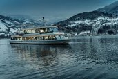Beleuchtetes Ausflugsschiff auf dem verschneiten Zeller See bei Dämmerung – stimmungsvolles Wintererlebnis nahe dem Familienhotel Amiamo.