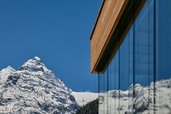 Aussenansicht der Hotelfassade mit Fenstern, in denen sich schneebedeckte Berge spiegeln, im Familienhotel Bella Vista in Suedtirol.