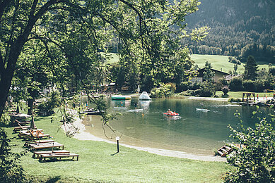 Badesee mit Liegen und Schwimmtrampolin im Familienhotel Post Family Resort im Salzburger Land.