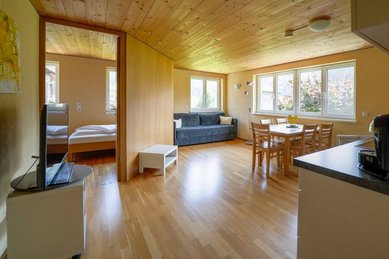 Heller Wohnbereich mit Esstisch, Sofa und Zugang zum Schlafzimmer im Familienhotel Sonne Bezau.