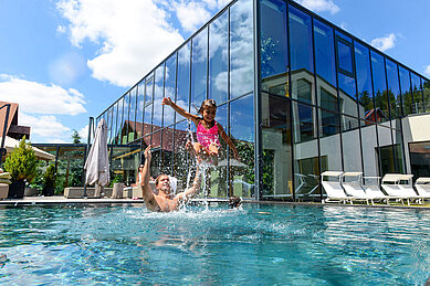 Familie planscht im großen Outdoor-Pool des Familienhotels Ulrichshof im Bayerischen Wald.